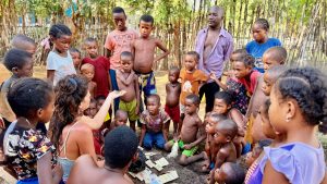 Photo de groupe sur laquelle Madame Tantely, entourée des écoliers, s'affaire à une explication sur les semences reproductibles. Dans sa main se trouvent des semences Kokopelli qu'elle montre aux enfants. Ce geste retient toute leur attention.