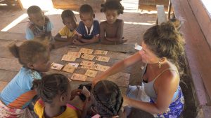 Photo de groupe sur laquelle apparaît Madame Tantely entourée des enfants de l'école dans laquelle elle intervient régulièrement. Des sachets de semences Kokopelli sont sur la table et elle s'affaire à une grande explication qui retient toute l'attention des enfants.